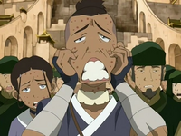 A group of people with red markings on their face are walking away from the the large city behind them. The young man in front is dressed in blue and is gripping his cheeks with an exaggerated expression on his face.